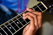 A smiling instructor showing a student how to position fingers on guitar strings.