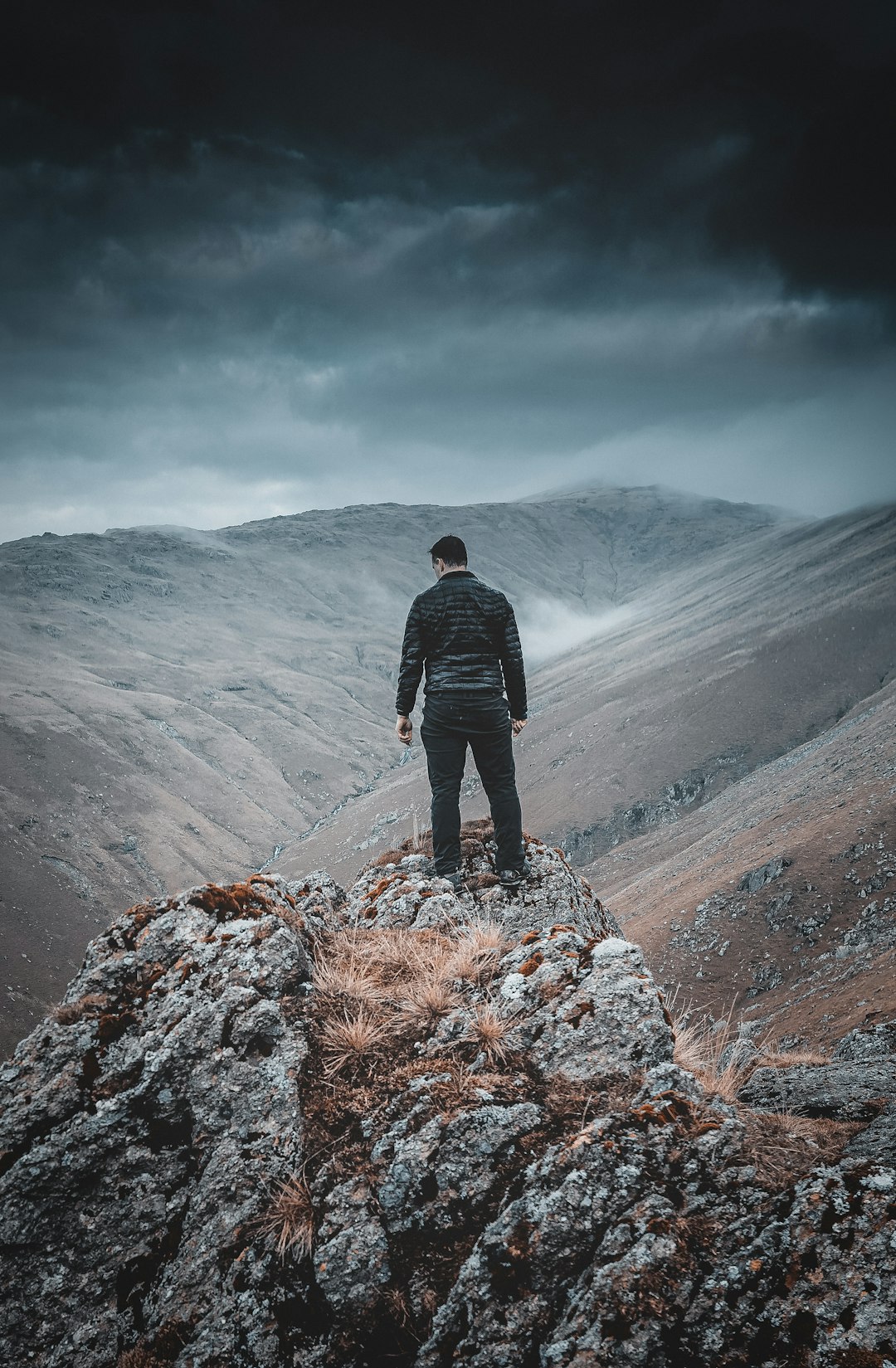 man in black jacket standing on rock mountain during daytime