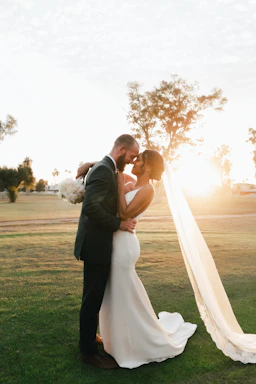 A warm, sunlit outdoor wedding scene with a couple sharing a genuine moment.