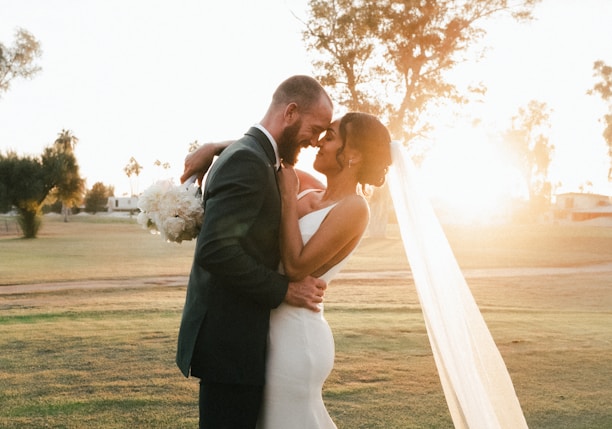 man and woman kissing on green grass field during sunset