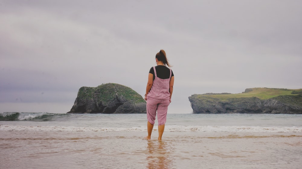 woman in pink dress standing on beach during daytime