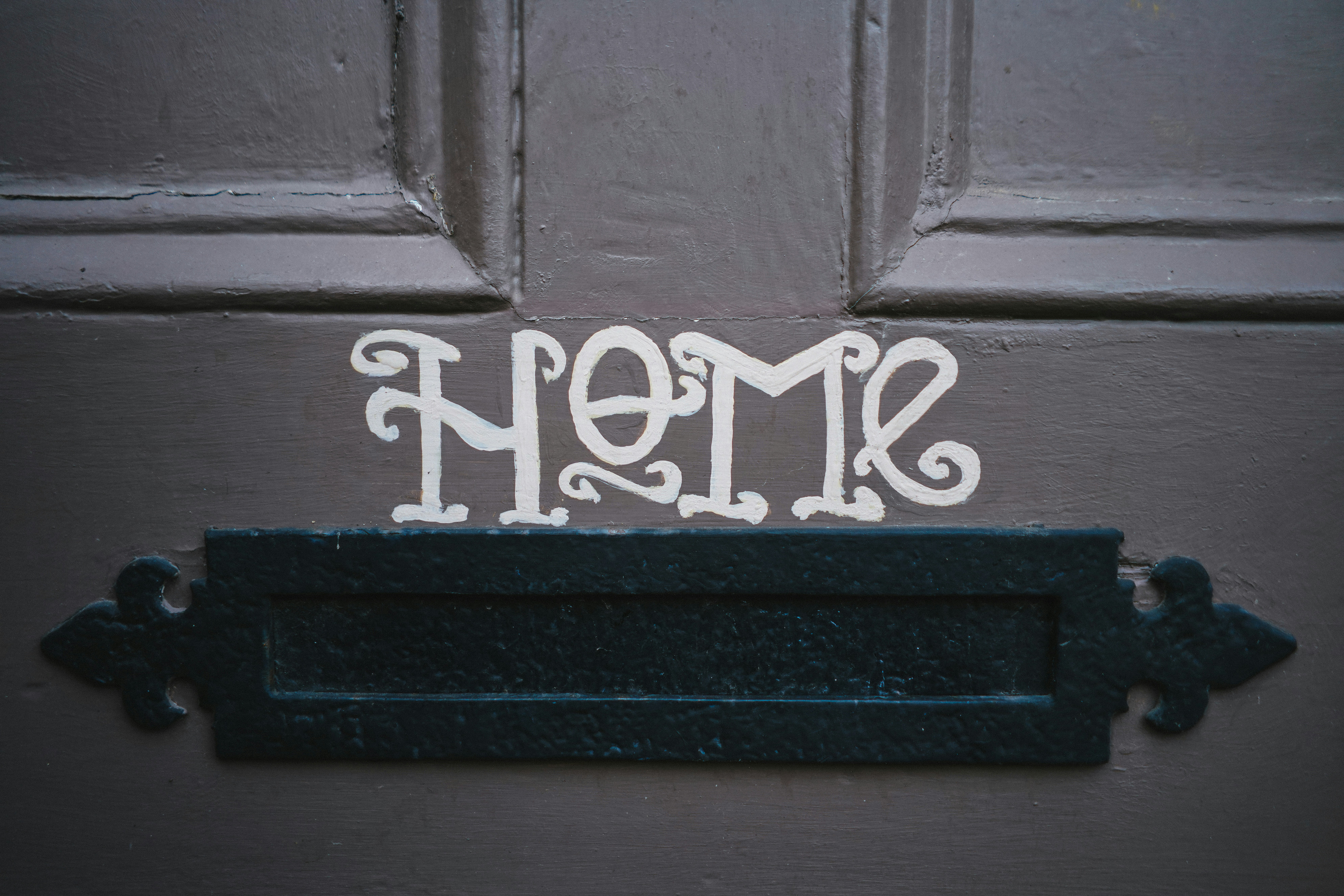 brown door with black mail slot and word home in white cursive