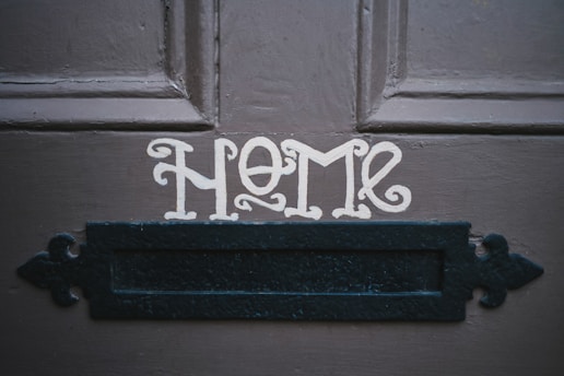 The word 'HOME' is painted in a decorative font on a dark wooden door above a black metal mail slot.