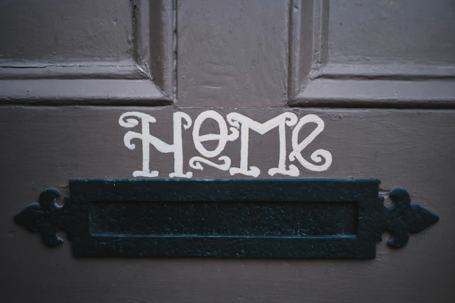 gray door with "home" painted in white and a mailbox slot in door