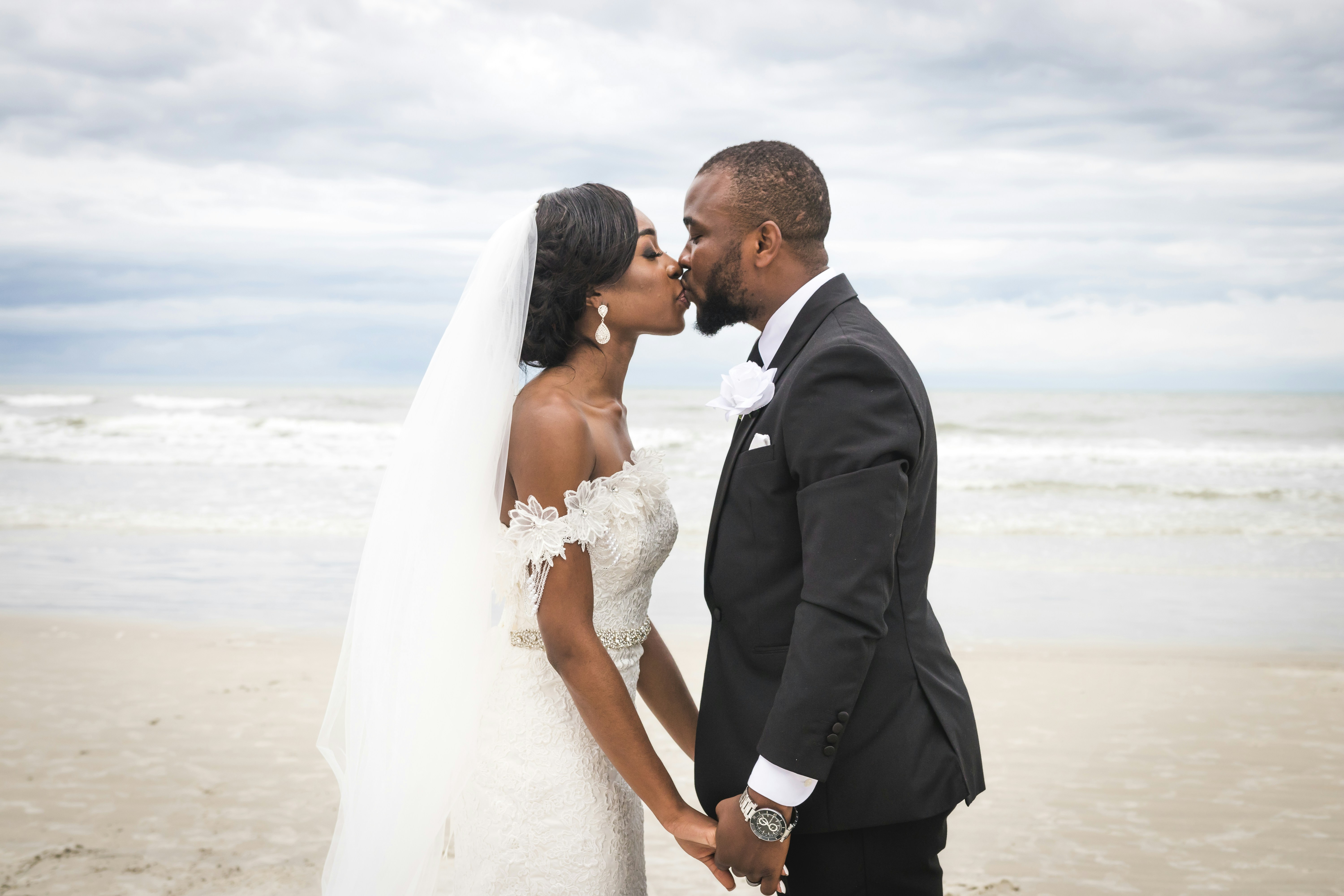 man-in-black-suit-kissing-woman-in-white-wedding-dress-on-beach-during-daytime