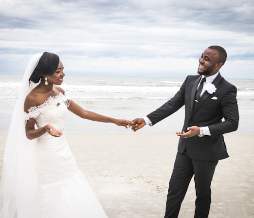 man in black suit holding hands with woman in white wedding dress on beach during daytime