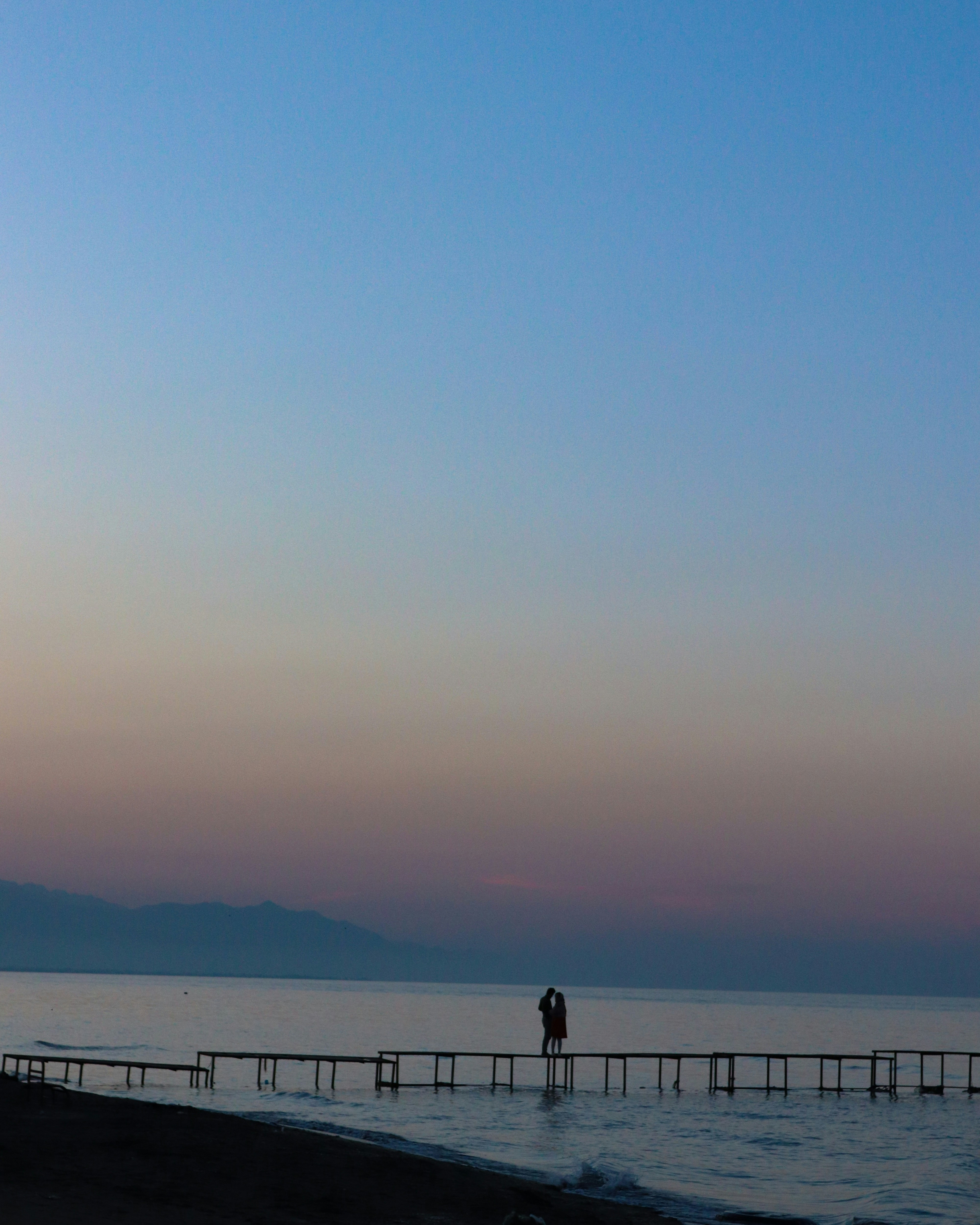 silhouette of 2 people standing on dock during sunset