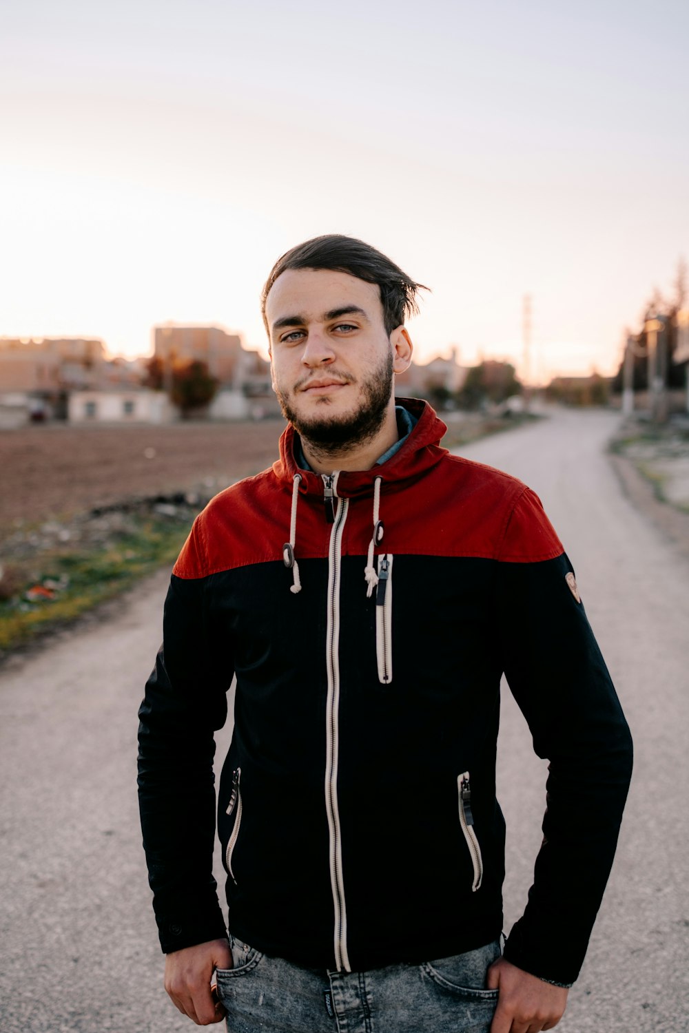 man in black and red hoodie standing on road during daytime