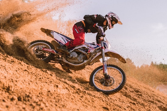 A rider in full gear navigating a rugged dirt trail on a powerful motocross bike under a clear blue sky.
