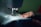 A hand gently holds fabric as it feeds through a sewing machine. The lighting is soft, focusing on the detailed stitching and the textile.