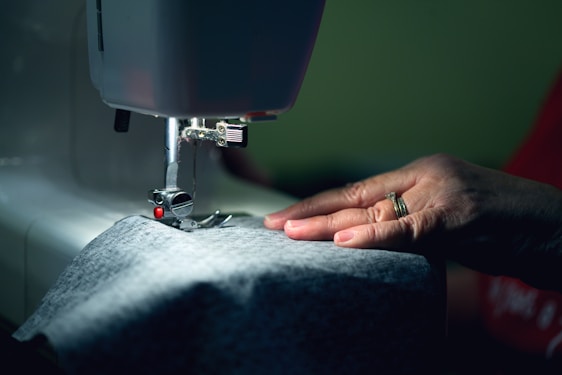 A skilled artisan hand-stitching a garment with rich Indian fabrics in a sunlit studio.