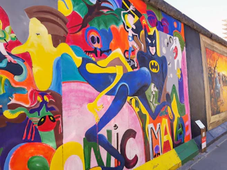 A vibrant street mural in Acapulco featuring bold cyan, yellow, and coral colors with comic-style characters laughing and pointing.