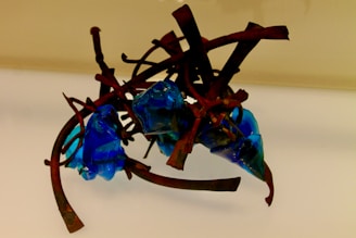 An abstract sculpture featuring intertwined, rust-colored metal rods combined with glossy, irregularly shaped blue glass elements.
