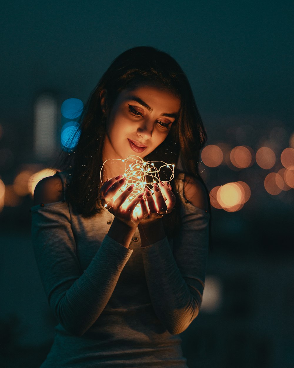 woman in blue long sleeved shirt holding lighted string lights