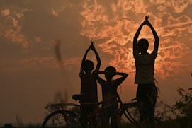 silhouette of 3 person standing beside bicycle during sunset