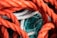 Interwoven ropes of various colors and textures. Thick orange ropes are primarily in the foreground, while white ropes with colored specks and thin blue-green nets are tangled together in the background.