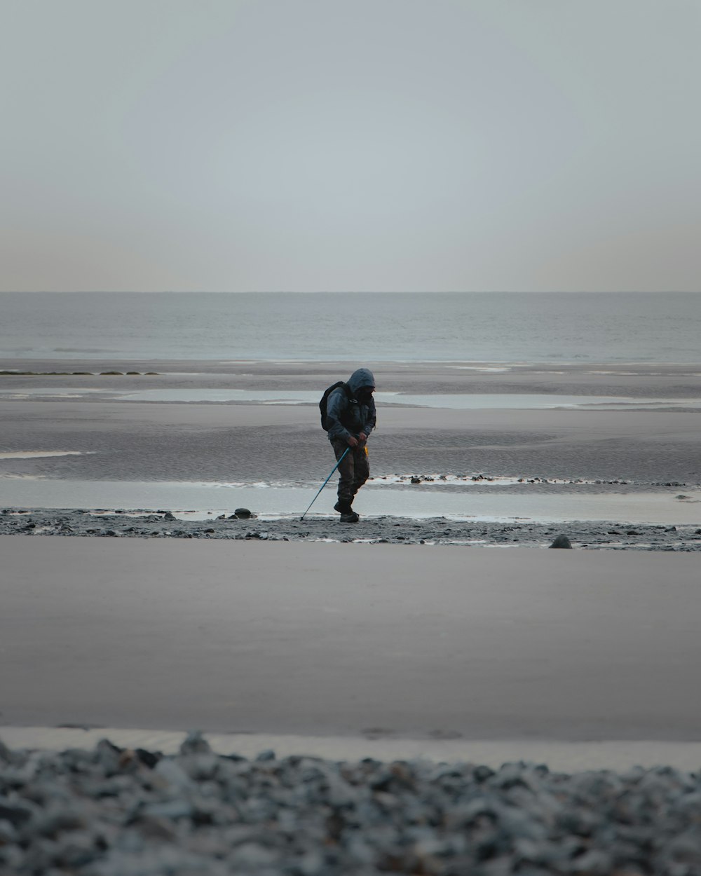 昼間のビーチを歩く黒いジャケットの男