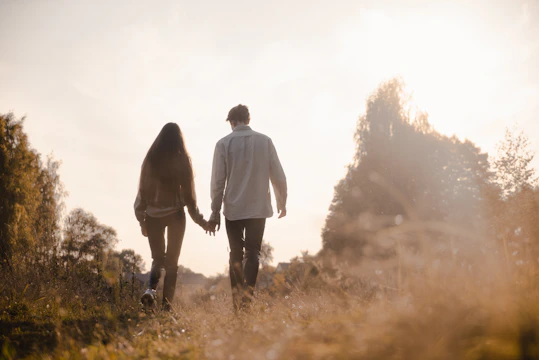 Cinematic shot of an authentic couple walking hand-in-hand along a charcoal-shadowed path at sunset.