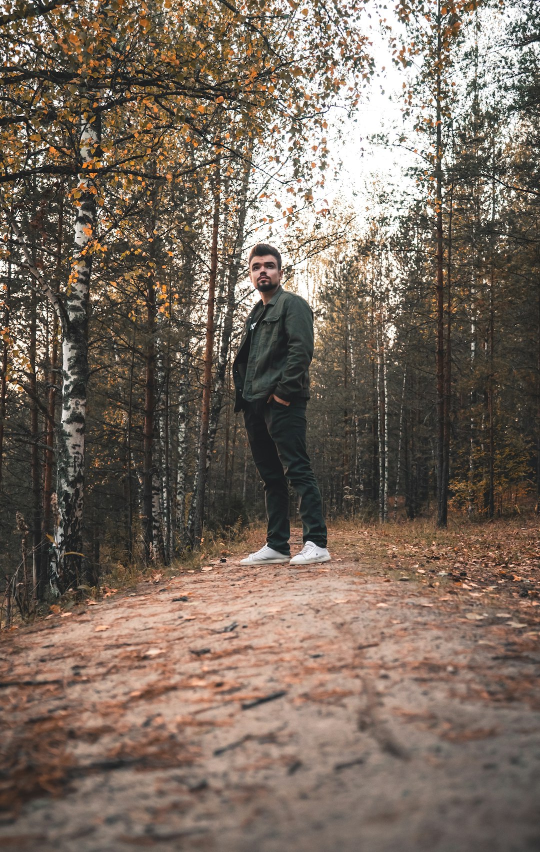 man in black jacket standing on brown dried leaves on forest during daytime