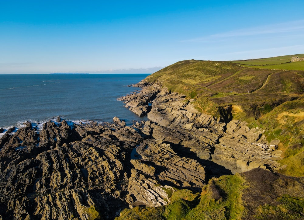 brown and green mountain beside blue sea under blue sky during daytime