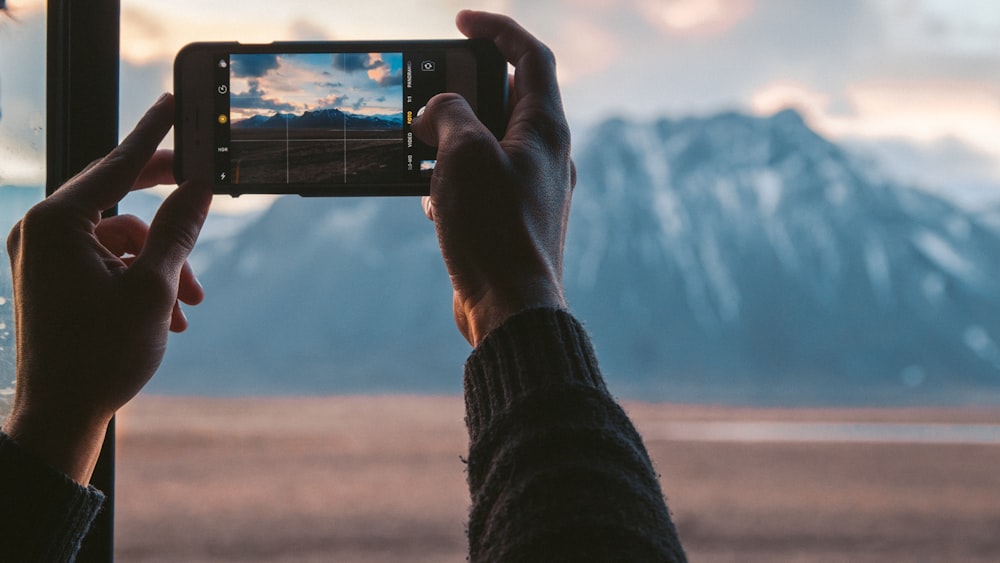 personne tenant un smartphone noir prenant une photo de la montagne pendant la journée