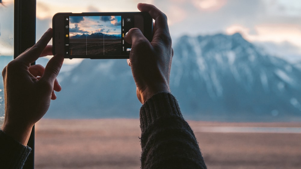 person holding black smartphone taking photo of mountain during daytime