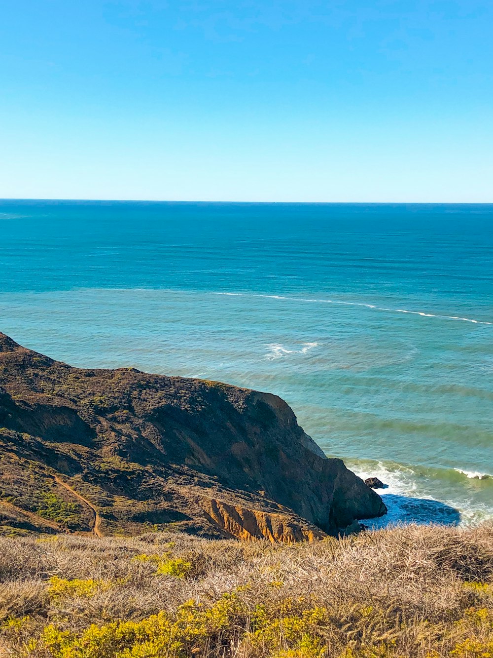 green and brown mountain beside blue sea during daytime