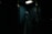 A person dressed as a ghost with a sheet over their head, standing inside a dimly lit telephone booth. The atmosphere is eerie, with minimal lighting highlighting the ghostly figure.