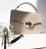 Bolso elegante color crema con herrajes dorados sutiles sobre tela neutra, accesorios de lujo Aura