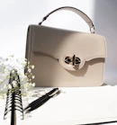 Close-up of a minimalist beige handbag resting on a soft ivory fabric.