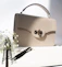 Close-up of a minimalist beige handbag resting on a soft ivory fabric.