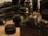 A collection of photography equipment is spread on a surface, including several camera lenses, a camera, a tripod, and camera bags. The focus is on the lenses, with some objects in the background appearing blurred due to the shallow depth of field.
