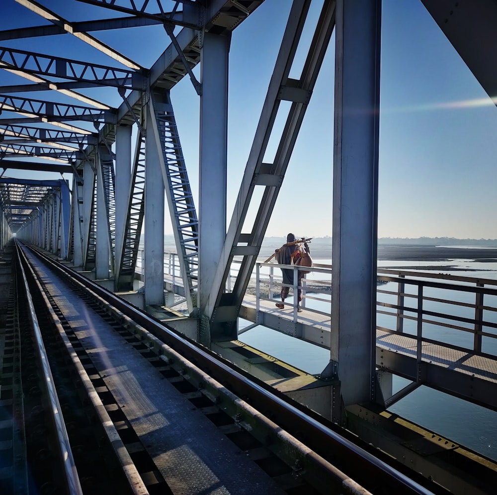 man in red shirt and black pants standing on gray metal bridge during daytime