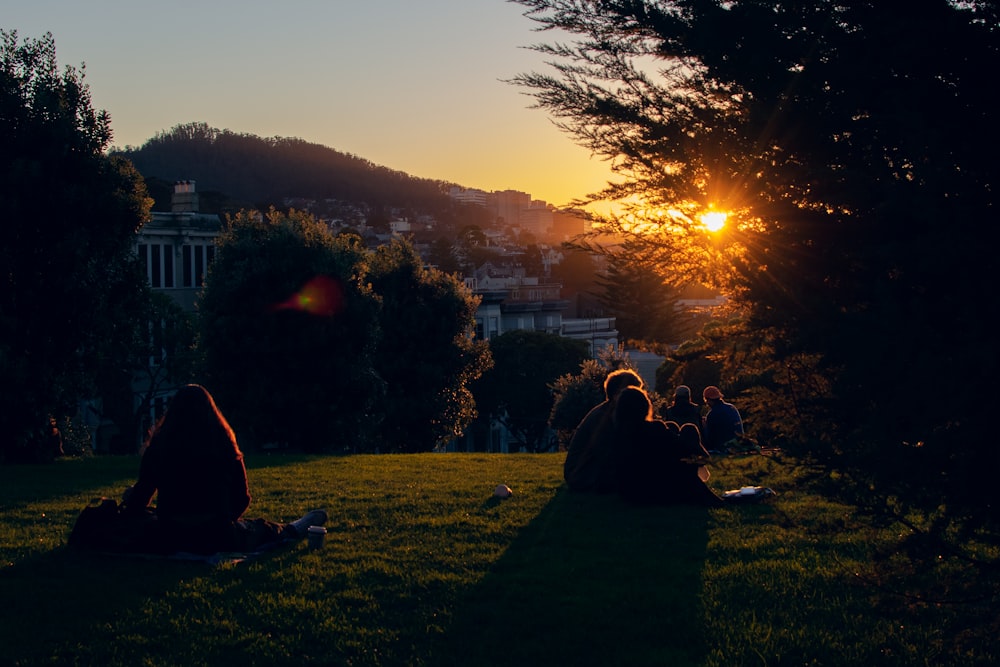 Menschen, die während des Sonnenuntergangs auf einem grünen Rasenfeld sitzen