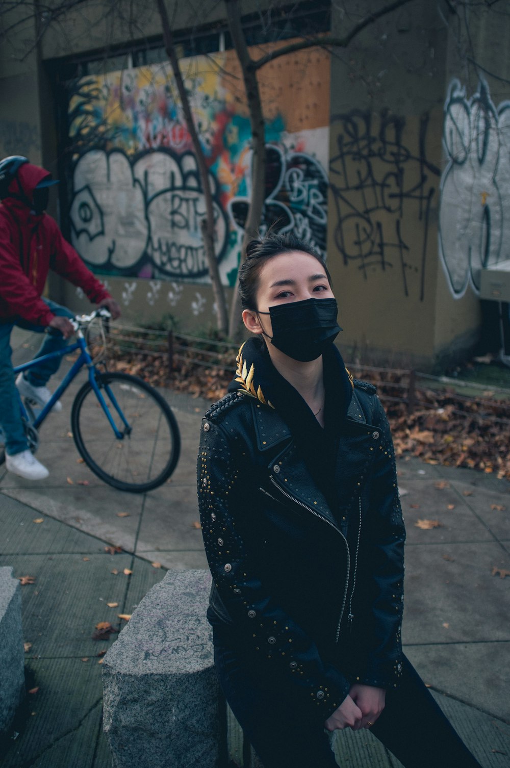 Frau in schwarzer Lederjacke und schwarzer Hose mit schwarzer Sonnenbrille neben blauem Fahrrad während