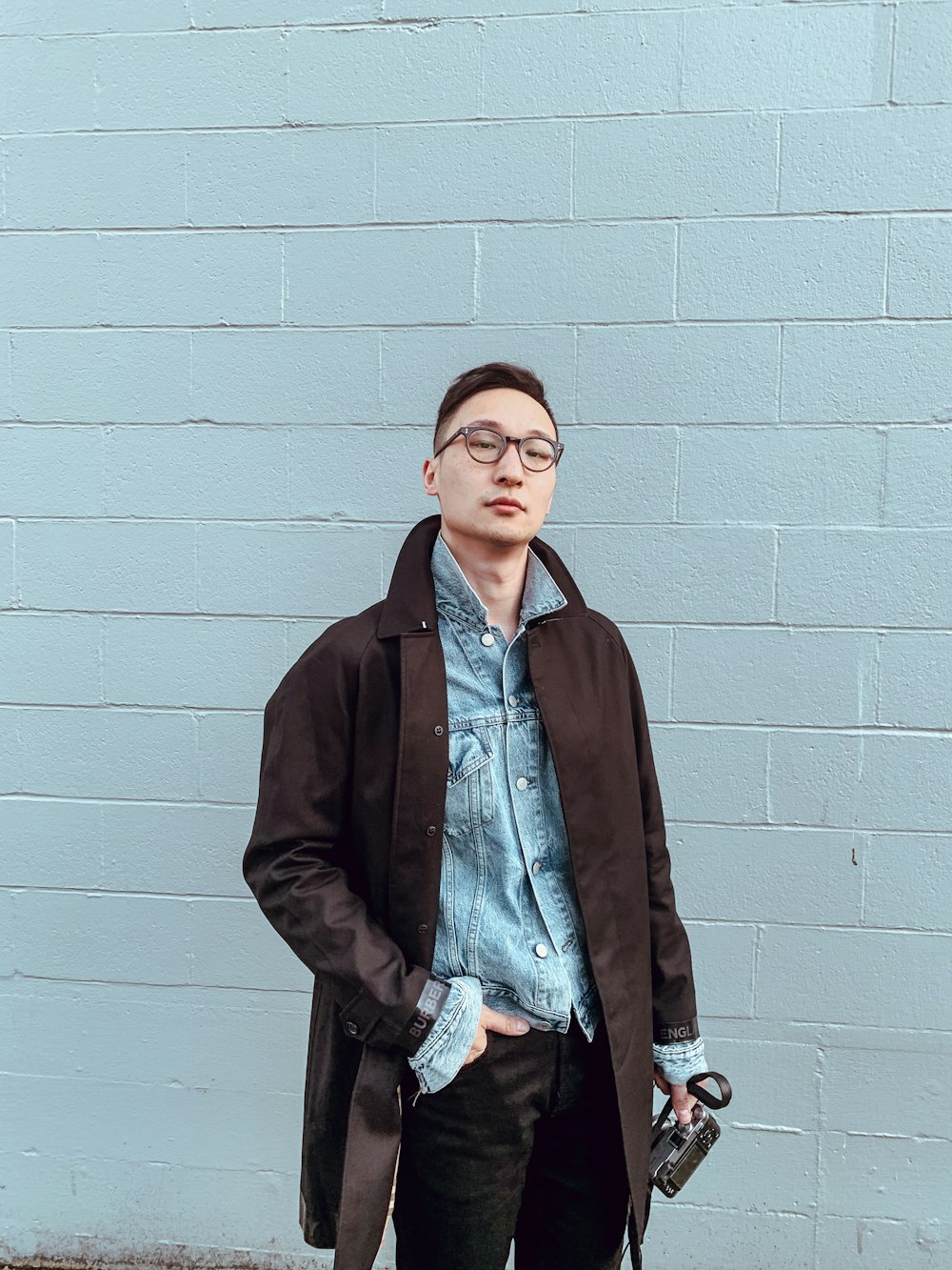 man in brown coat standing beside white wall