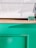 A minimalistic setup featuring a white countertop surface and a wooden edge. Below is a vibrant green panel, likely part of a counter or kiosk. A small green placard with text sits near the corner of the white surface.