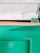A minimalistic setup featuring a white countertop surface and a wooden edge. Below is a vibrant green panel, likely part of a counter or kiosk. A small green placard with text sits near the corner of the white surface.