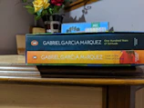 A collection of Gabriel García Márquez's books stacked on a wooden table.