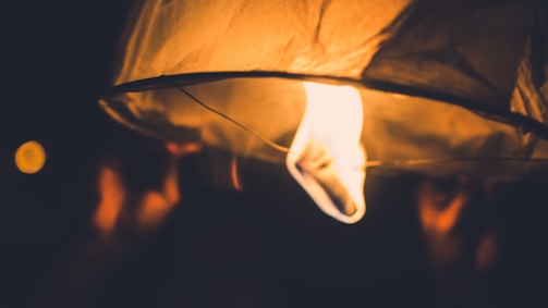 Close-up of hands holding a glowing lantern in the dark.