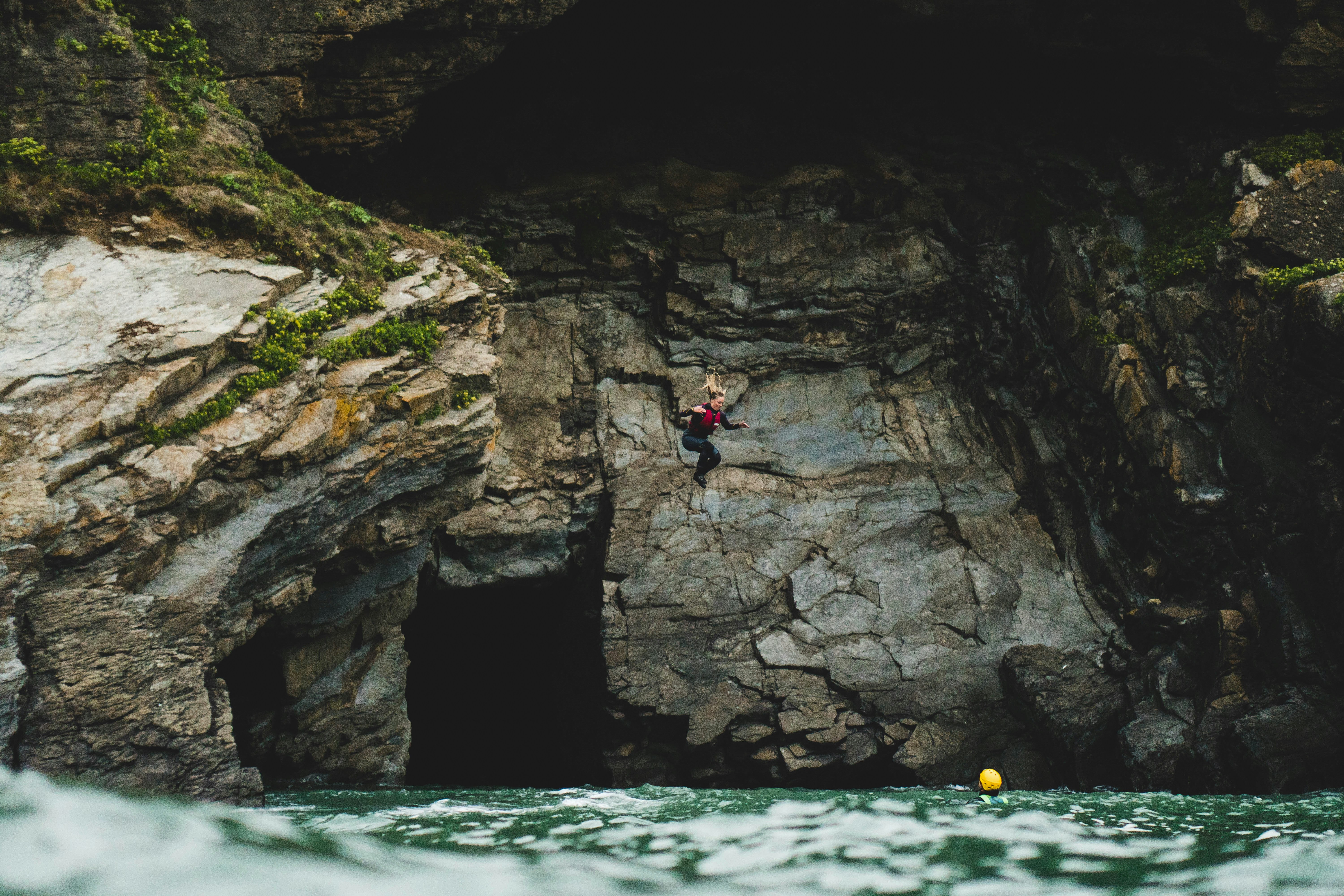 person in blue shirt and black pants standing on rock formation near body of water during