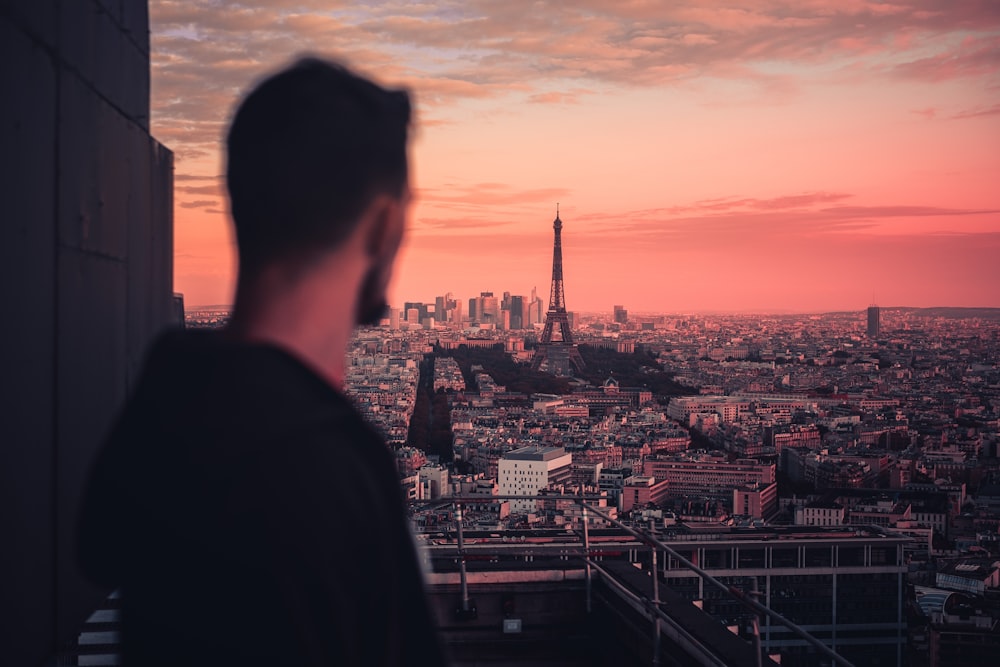 homme en veste noire regardant les bâtiments de la ville au coucher du soleil