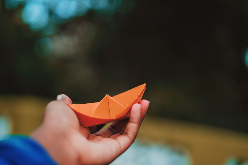 person holding orange paper boat