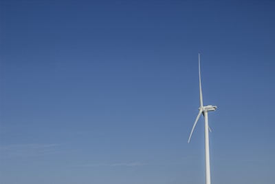 A sleek wind turbine spinning gracefully against a clear blue sky near the ocean.