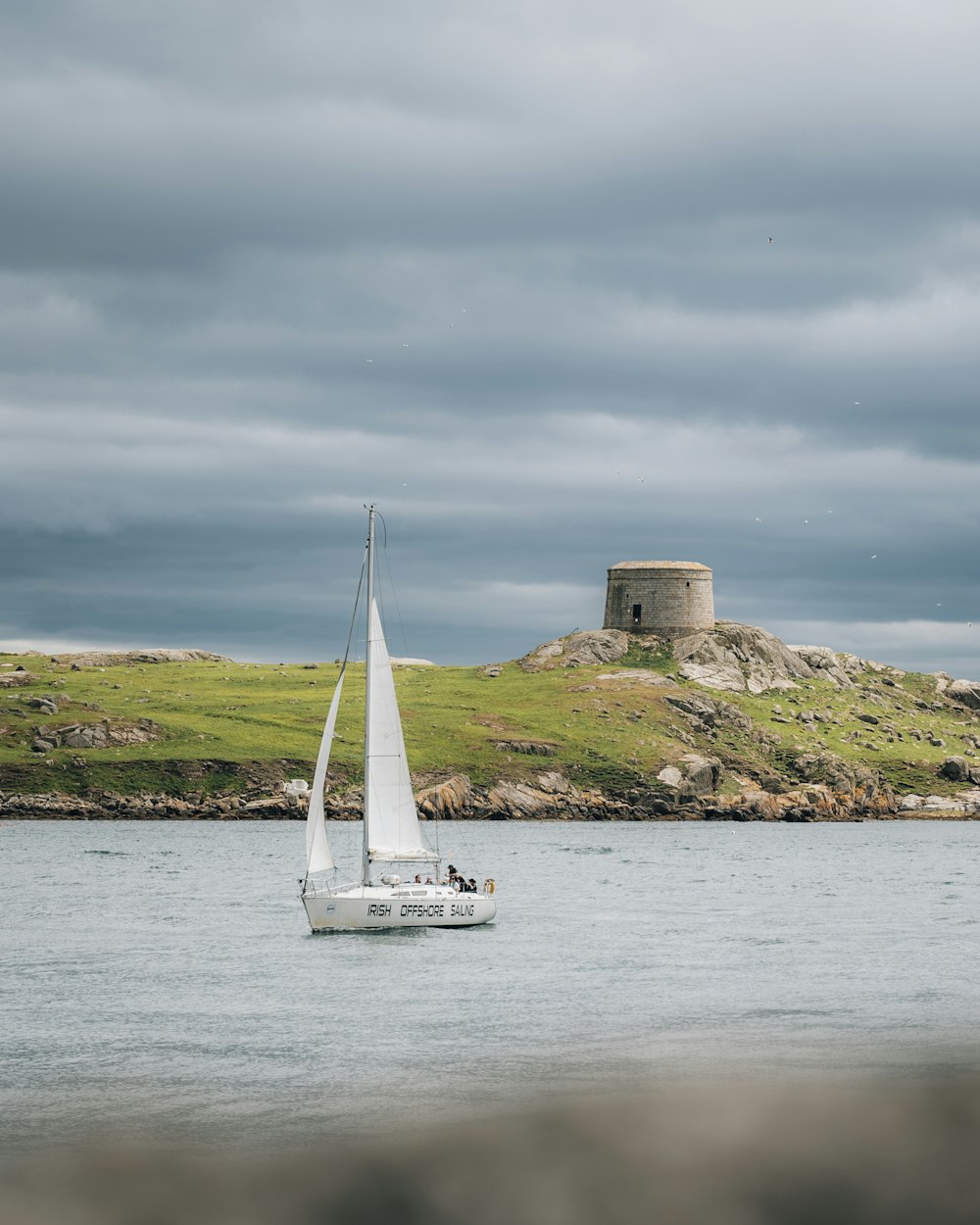 white sailboat on sea near brown concrete building under white clouds