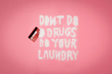 A pink background with a red credit card on the left. White powder spelling out 'DON'T DO DRUGS DO YOUR LAUNDRY' is arranged in the middle.