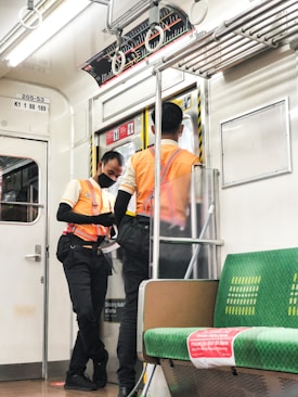 man in orange and black jacket and black pants standing beside white and green train during