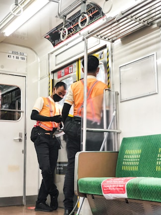 man in orange and black jacket and black pants standing beside white and green train during