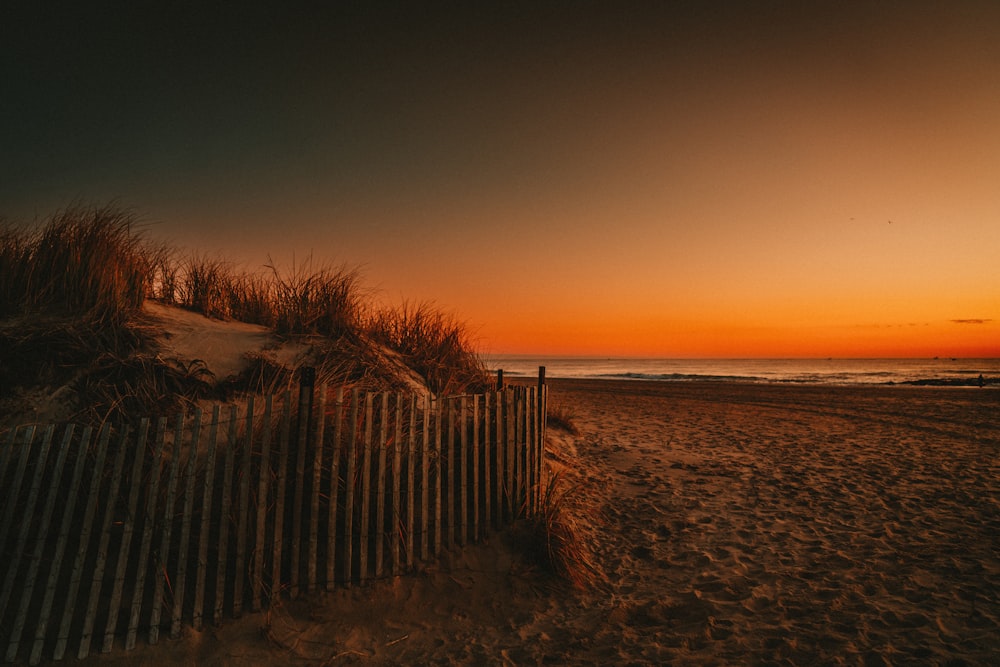 brown wooden fence on brown sand near body of water during sunset