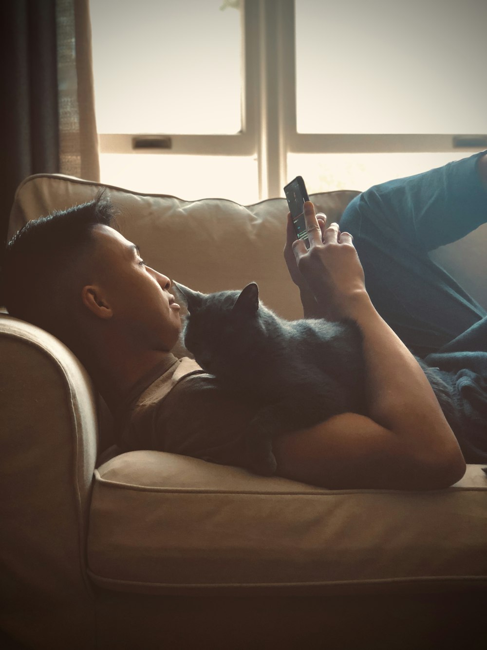 woman in blue tank top lying on couch with black cat
